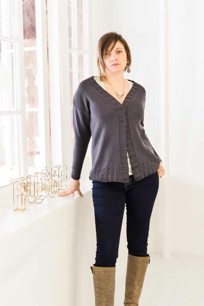 A woman in a straight-sided drop shoulder cardigan next to a window.