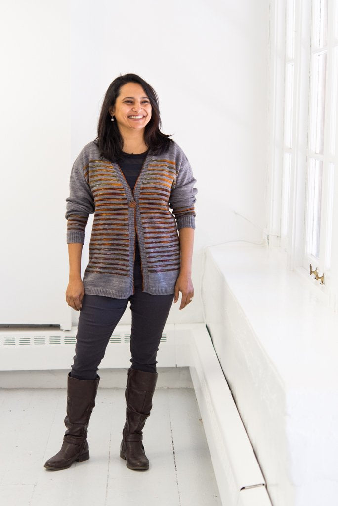 Woman smiling next to a window wearing a striped drop-shoulder cardigan.